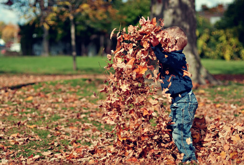 Kind dat met herfstbladeren gooit, een van de herfstactiviteiten van dit lijstje