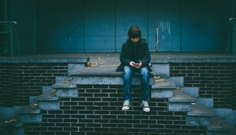 cyberpesten / kind zit op muurtje met telefoon